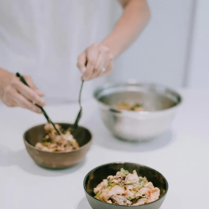 Schalen mit frisch zubereitetem Mittagessen von einem Koch stehen auf dem Tisch. Mit Besteck rührt jemand in einer der Schüsseln.