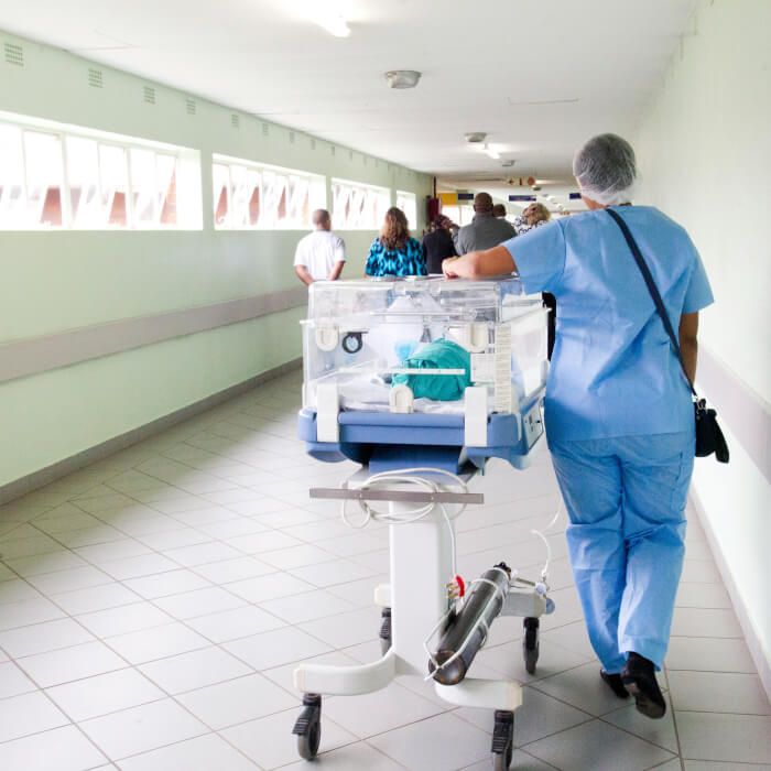 Krankenpflegehelferin schiebt ein neugeborenes Baby durch den Krankenhausflur.