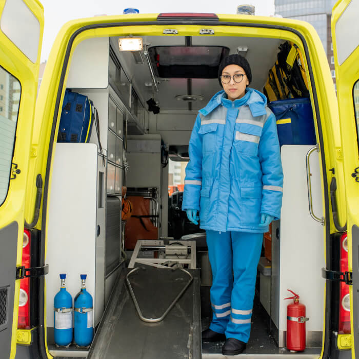 heiße Notfallsanitäterin in einem Krankenwagen bei der Arbeit. Trägt dabei komplett blaue Arbeitsklamotten.