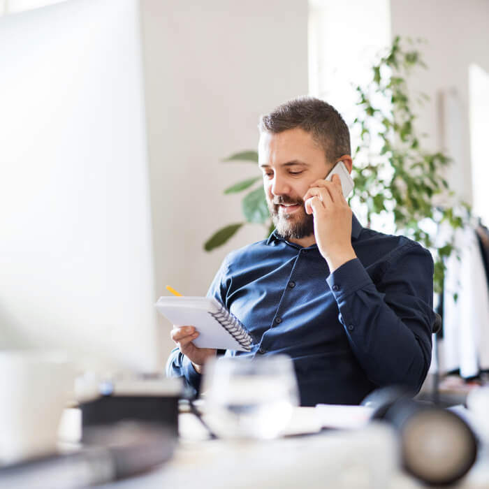 Unternehmer im Büro. Er telefoniert gerade mit wichtigen Geschäftspartnern und hält einen Notizblock bereit.