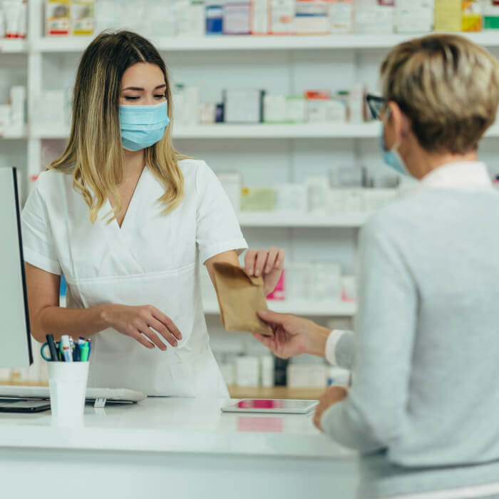 Bild einer Apothekerin, die einer Patientin / Kundin gerade ein verschreibungspflichtiges Medikament über der Ladentheke gibt. Die Krankenkasse verlang 5 Euro Zuschuss für die Pillen, die in Asien hergestellt wurden und dessen Produktion vermutlich 17 Cent gekostet hat.