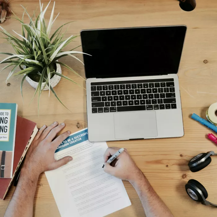 Schreibtisch mit Computer, Pflanze, Kopfhörern und einem Mann, der als Marketingmanager zuständig ist, schreibt auf Papier